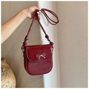 Detail of burgundy PU crossbody bag featuring a decorative silver metallic bow clasp