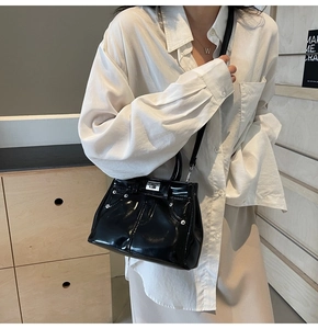 Détail d'un sac à main noir verni avec rivets argentés et fermoir rotatif classique sur bandoulière