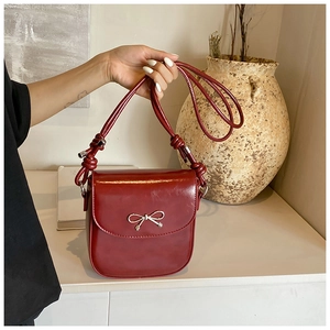 Detail of burgundy saddle bag with silver metal bow and knotted strap design