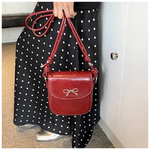 Close-up of a glossy red PU handbag featuring a silver metal bow and stylish knotted shoulder strap