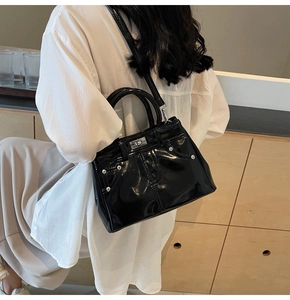 Détail du sac à main en cuir verni noir avec boucles argentées porté par un mannequin