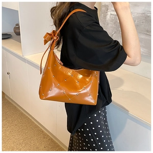 Détail du sac bandoulière matelassé caramel avec clous et nœud sur la sangle