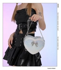 Detail of holographic heart-shaped bag with metal bow and silver ball chain strap