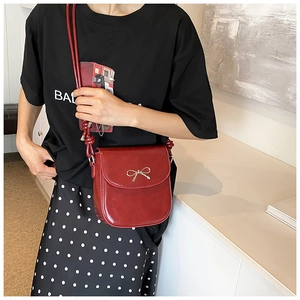 Detail of red PU leather crossbody bag featuring a decorative golden metal bow on the flap