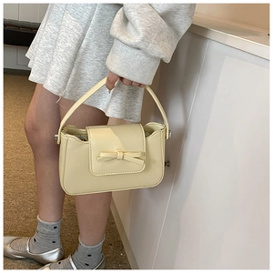 Detail view of mini cream yellow PU leather handbag with decorative leather bow and metal buckle