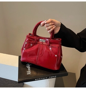 Détail du sac à main rouge brillant avec fermoir argenté et rivets sur un livre