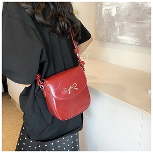 Detail of red PU leather crossbody bag featuring a golden metal bow buckle and knotted strap
