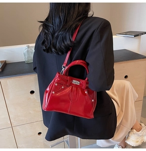 Détail du sac à bandoulière en cuir verni rouge avec rivets argentés porté par le modèle
