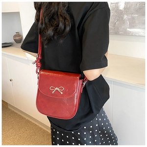 Detail of red PU leather crossbody bag with gold bow clasp and knotted strap design