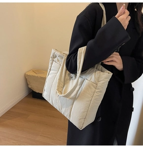 Close-up of a cream quilted tote bag featuring a vertical padded design and wide handles