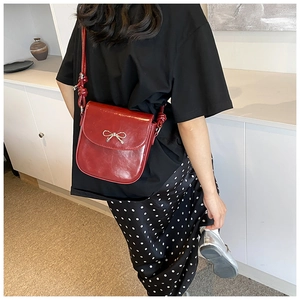 Detail of red faux leather crossbody bag with silver bow and knotted strap on model