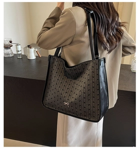 Model wearing dark coffee canvas tote bag with leather trim and metal bow detail
