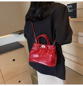Détail d'un sac bandoulière rouge verni avec rivets argentés sur un blazer noir