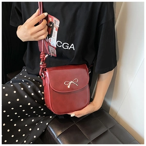 Detail of wine red crossbody bag with golden bow hardware and knotted shoulder strap