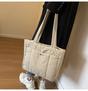 Detail view of a beige quilted nylon tote bag with shoulder straps and metal buckle front pocket