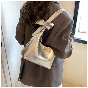 Détail du sac argenté métallisé avec rivets et un grand nœud sur la bandoulière réglable