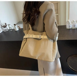 Detail of khaki canvas tote bag featuring a decorative cream strap with silver buckle