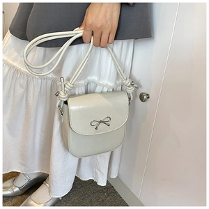 Close-up of minimalist beige PU leather crossbody bag featuring a golden metal bow buckle