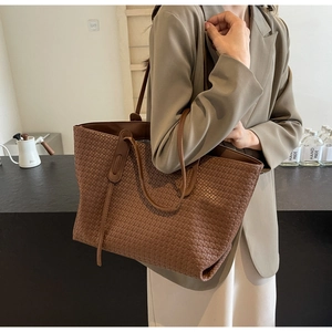 Detail of a brown woven PU leather tote bag worn on shoulder by a model for daily use