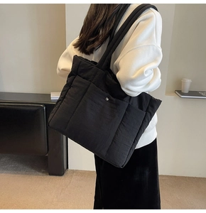 Detail view of a black quilted tote bag with padded nylon texture and metal snap pocket