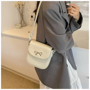 Cream PU crossbody bag with silver bow and knot strap details shown on a model