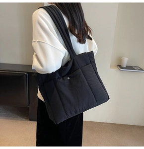 Close-up of black quilted puffer tote bag with side pocket and silver snap button detail