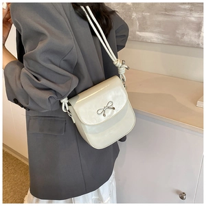 Detail of cream white PU leather crossbody bag with silver metal bow and knotted strap