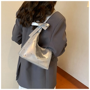 Détail du sac bandoulière argenté métallisé avec rivets et nœud sur une veste gris foncé