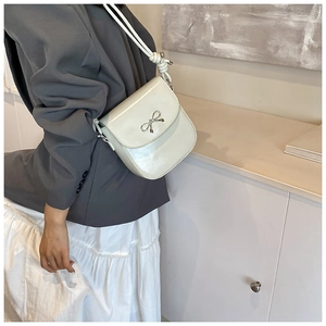 Detail of white PU leather crossbody bag featuring a silver metal bow and knotted strap