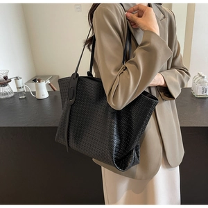 Detail of hand-woven black PU leather tote bag shown with a stylish casual outfit