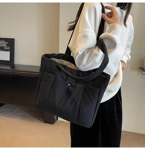 Detail view of black quilted puffer tote bag with front metal snap pocket and padded straps