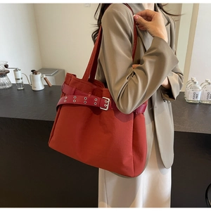 Detailed view of a red fabric tote bag featuring decorative belt straps and metal eyelets