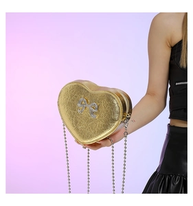 Detail of a heart-shaped gold PU leather crossbody bag with sparkling rhinestone bow