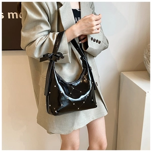 Détail d'un sac à main en cuir verni noir avec clous argentés et nœud décoratif