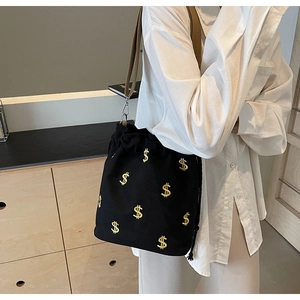 Détail du sac seau en toile noire avec broderie de signes dollar dorés et bandoulière large