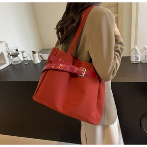 Detail of red canvas tote bag with decorative strap and silver metal buckle worn by model