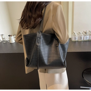Detail of black woven leather tote bag shoulder strap shown on model in modern setting