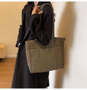 Olive green quilted puffer tote bag shown on model featuring a silver metal buckle front pocket