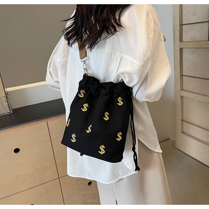 Détail du sac seau noir en toile avec signes dollar dorés et bandoulière réglable
