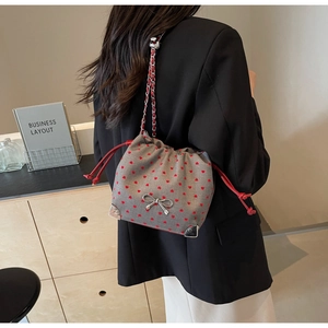 Detailed view of gray felt bucket bag with red hearts and metal chain strap on model