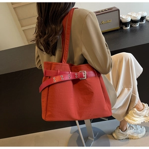 Detail of vibrant orange nylon tote bag featuring decorative belt buckle and shoulder strap