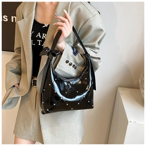 Détail du sac en cuir verni noir avec motif matelassé, clous argentés et nœud décoratif