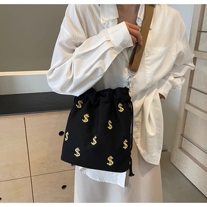 Détail d'un sac seau en toile noire avec broderie dollar et large bandoulière en toile
