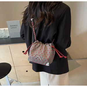 Detail of grey fabric crossbody bag featuring red heart patterns and silver bow decoration