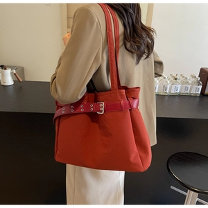 Detail of brick red canvas tote bag with leather strap and silver buckle on model