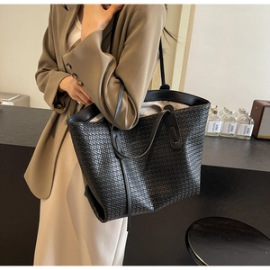 Side view of a large black woven PU leather tote bag worn by a model in a beige outfit