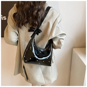 Détail d'un sac à bandoulière en cuir verni noir avec clous argentés et nœud décoratif