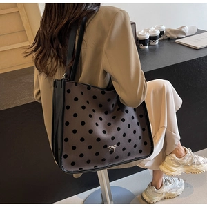 Brown tote bag with black polka dots and metal bow detail shown on model in urban setting