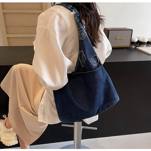 Détail d'un grand sac fourre-tout en denim bleu avec broderie de rose sur un mannequin