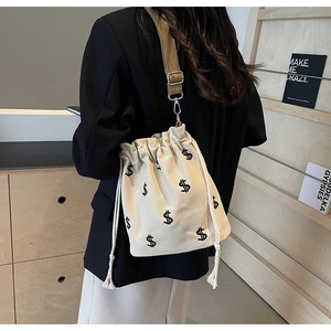Détail du sac seau en toile avec broderie signe dollar et large bandoulière